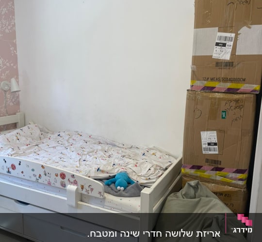 מיטה עם מצעים, קופסאות קרטון ושק פוף בחדר ילדים